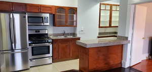 Kitchen featuring stainless steel appliances, glass insert cabinets, brown cabinets, and light tile patterned floors