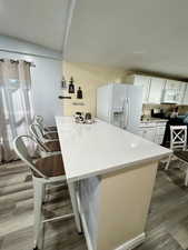 Kitchen featuring white cabinets, a quartz breakfast bar area, light stone counters, white appliances, and dark wood-style floors