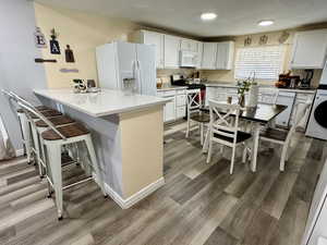 Kitchen featuring a quartz kitchen breakfast bar, white appliances, white cabinetry, light stone counters, and recessed lighting