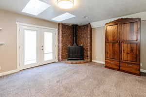 Unfurnished living room featuring a wood stove, a textured ceiling, light carpet, french doors, and a skylight