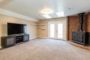 Unfurnished living room with a wood stove, a textured ceiling, light carpet, french doors, and a skylight