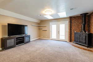 Unfurnished living room with a wood stove, a textured ceiling, light carpet, french doors, and a skylight