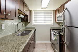 Kitchen featuring stainless steel appliances, light tile patterned floors, dark brown cabinetry, tasteful backsplash, and a textured ceiling