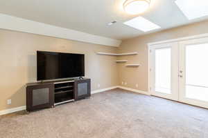 Unfurnished living room with french doors, a skylight, light colored carpet, a textured ceiling, and lofted ceiling