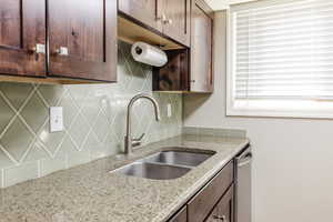 Kitchen with backsplash, dark brown cabinets, light stone countertops, and dishwasher