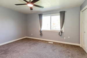 Empty room featuring carpet flooring, a textured ceiling, and a ceiling fan