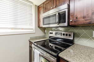 Kitchen with appliances with stainless steel finishes, light stone counters, backsplash, and dark brown cabinetry