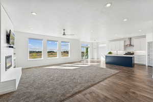 Unfurnished great room with a fireplace, ceiling fan, dark wood finished floors, recessed lighting, and a chandelier