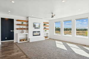 Unfurnished living room with a large fireplace, recessed lighting, a ceiling fan, built in features, and carpet floors