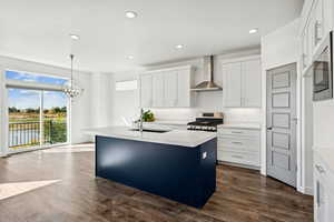 Gourmet Kitchen featuring an island with sink, decorative light fixtures, recessed lighting, wall chimney exhaust hood, and dark wood finished floors