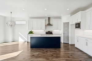 Kitchen with white cabinetry, an island with sink, medium wood-style flooring, wall chimney exhaust hood, and recessed lighting