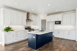 Kitchen featuring white cabinetry, wall chimney range hood, recessed lighting, a kitchen island with sink, and  medium  wood-style flooring