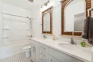 Full bath with washtub / shower combination, double vanity, and light tile patterned floors