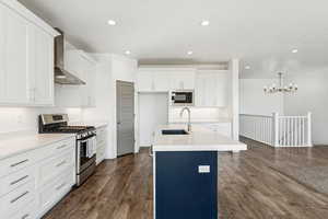 Kitchen featuring stainless steel gas range, white cabinetry, a center island with sink, wall chimney range hood, and medium wood-style flooring