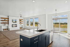 Kitchen featuring hanging light fixtures, a center island with sink, a large fireplace,  wood-type flooring, and recessed lighting