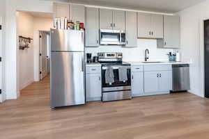 Kitchen with appliances with stainless steel finishes, light wood-style flooring, and gray cabinetry