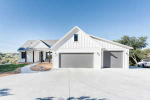 Modern farmhouse style home with board and batten siding, covered porch, roof with shingles, driveway, and an attached garage