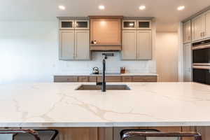 Kitchen with light stone counters, recessed lighting, double oven, a kitchen bar, and gray cabinets