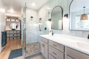 Bathroom with double vanity, a shower stall, light wood-type flooring, and tasteful backsplash