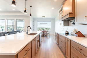 Kitchen featuring light stone countertops, light wood finished floors, recessed lighting, pendant lighting, and glass insert cabinets