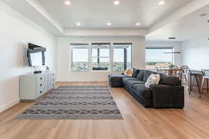 Living area with a raised ceiling, healthy amount of natural light, light wood-style flooring, and recessed lighting