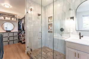 Full bathroom with a spacious closet, vanity, a shower stall, and light wood finished floors