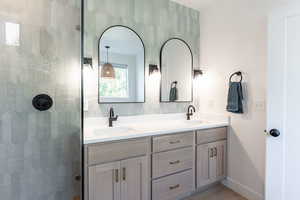 Full bath featuring double vanity, tiled shower, and light wood finished floors