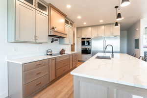 Kitchen with light stone counters, glass insert cabinets, hanging light fixtures, and recessed lighting
