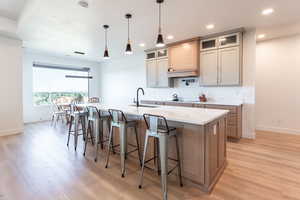 Kitchen with glass insert cabinets, a kitchen bar, a large island with sink, pendant lighting, and light stone counters
