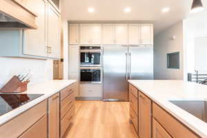 Kitchen featuring under cabinet range hood, appliances with stainless steel finishes, light wood finished floors, recessed lighting, and light stone counters