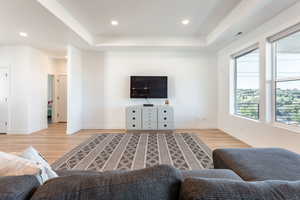 Living area featuring a raised ceiling, recessed lighting, and light wood finished floors