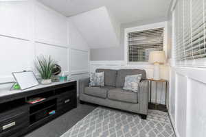 Sitting room featuring a decorative wall, carpet flooring, a wainscoted wall, and lofted ceiling