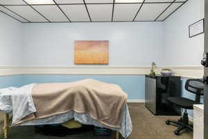 Carpeted bedroom featuring a drop ceiling and freestanding refrigerator