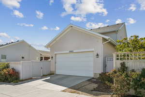 View of side of property featuring driveway, stucco siding, a garage, and a gate