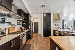 Kitchen with open shelves, stainless steel appliances, light wood-style floors, recessed lighting, and wall chimney exhaust hood