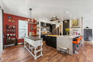 Kitchen featuring dark wood-style flooring, dark cabinets, a kitchen breakfast bar, light stone countertops, and stainless steel fridge