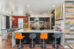 Kitchen featuring a breakfast bar area, appliances with stainless steel finishes, dark wood finished floors, a peninsula, and wall chimney range hood
