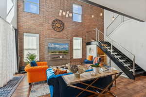 Living room with a towering ceiling, dark wood finished floors, brick wall, and stairs