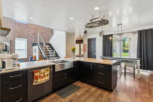 Kitchen with dark cabinetry, brick wall, dishwasher, dark wood-style flooring, and decorative light fixtures