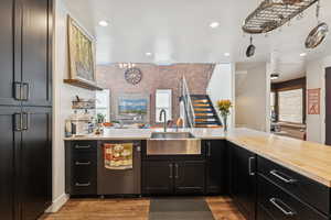 Kitchen featuring dark cabinets, dishwasher, dark wood finished floors, recessed lighting, and brick wall