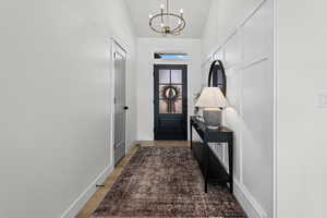 Doorway with lofted ceiling, wood finished floors, and a chandelier