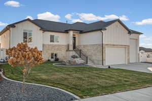 View of front of house with board and batten siding, stone siding, a front lawn, and driveway