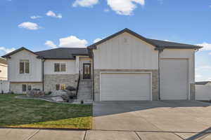 View of front of home with board and batten siding, driveway, a front lawn, an attached garage, and stone siding