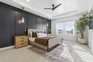 Carpeted bedroom featuring a decorative wall, a tray ceiling, and a ceiling fan