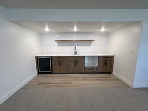 Indoor wet bar featuring beverage cooler, open shelves, light carpet, and dark brown cabinetry