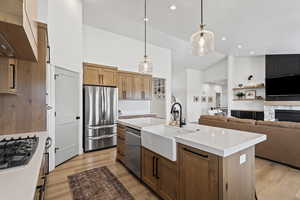 Kitchen with brown cabinetry, open floor plan, pendant lighting, high vaulted ceiling, and an island with sink
