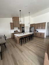 Kitchen with a breakfast bar, decorative backsplash, decorative light fixtures, a large island with sink, and a textured ceiling