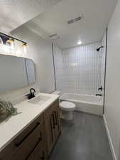 Bathroom featuring shower / washtub combination, vanity, a textured ceiling, and dark tile patterned flooring