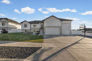 View of front of property with board and batten siding, stone siding, a garage, concrete driveway, and a gate