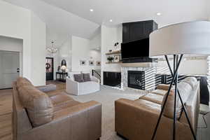 Living area with high vaulted ceiling, a chandelier, a stone fireplace, and recessed lighting